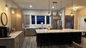 A modern kitchen with a large island, wooden cabinets, and pendant lighting. - Finger Lake Retreat (Prattsburgh)