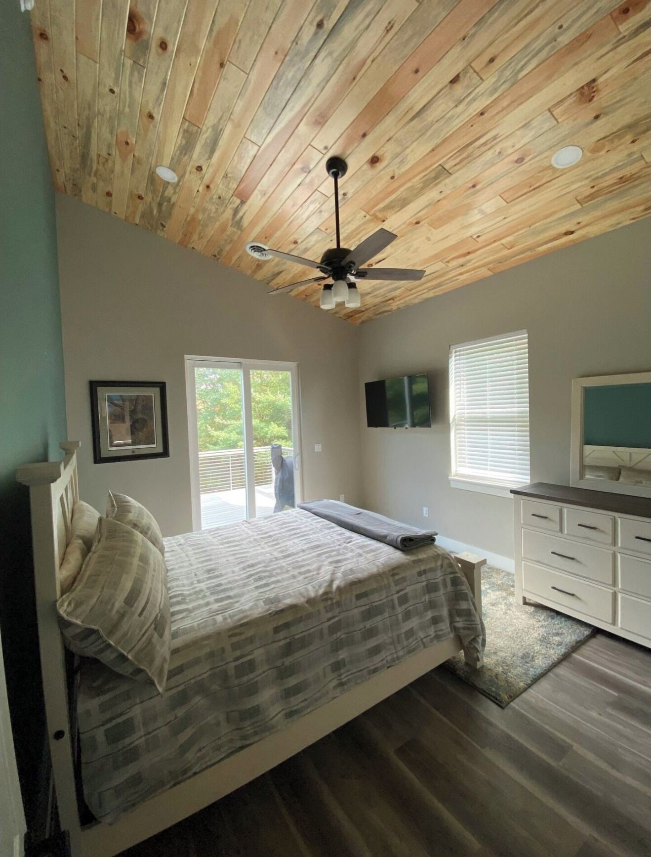 Une chambre à coucher avec un lit, un ventilateur de plafond, une commode et un téléviseur.