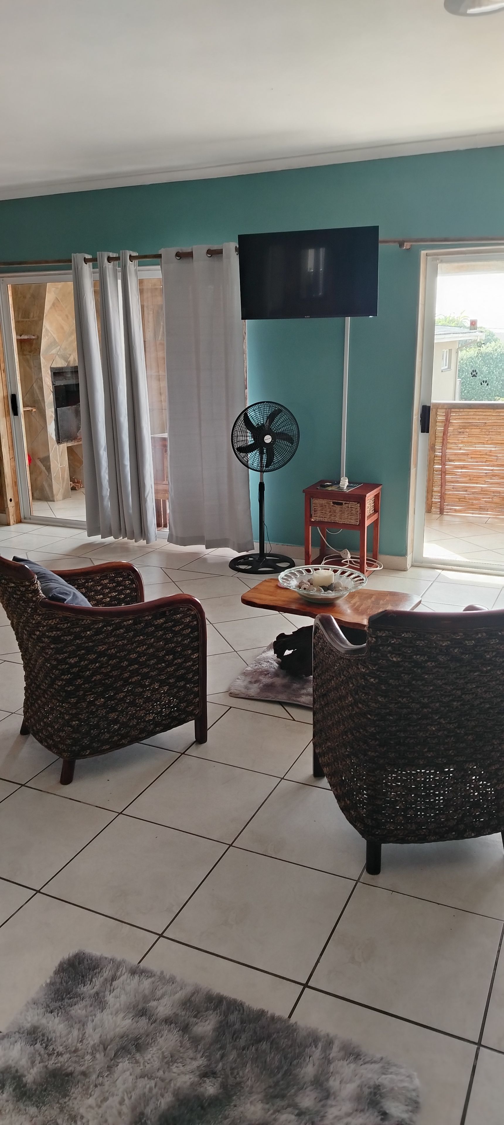 A living room with two wicker chairs, a TV, a fan, and a small table with a bowl.