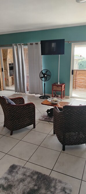Una sala de estar con dos sillones de mimbre, un televisor, un ventilador y una mesita con un tazón.