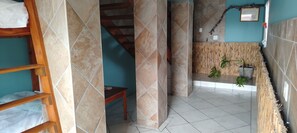 Una habitación con una cama litera de madera, una escalera y un muro de bambú.