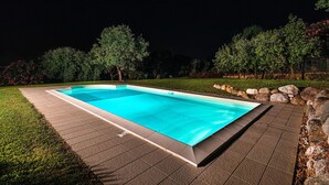 A rectangular swimming pool with a tiled deck, surrounded by a grassy area and trees. - Villa Elisa with pool (Padenghe sul Garda)