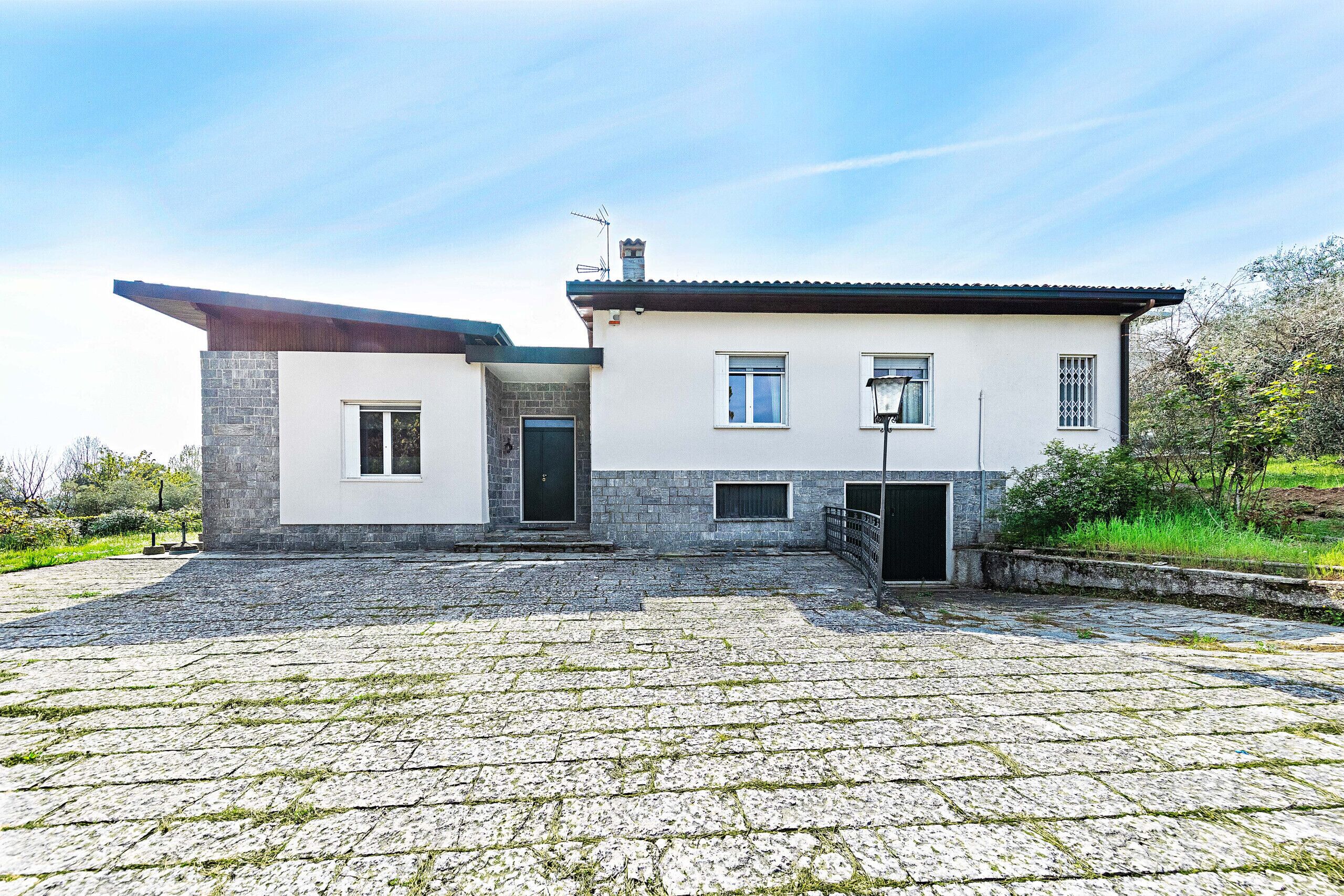 Une maison moderne à deux étages, dotée d’une façade en pierre, d’un toit plat et d’une allée pavée.