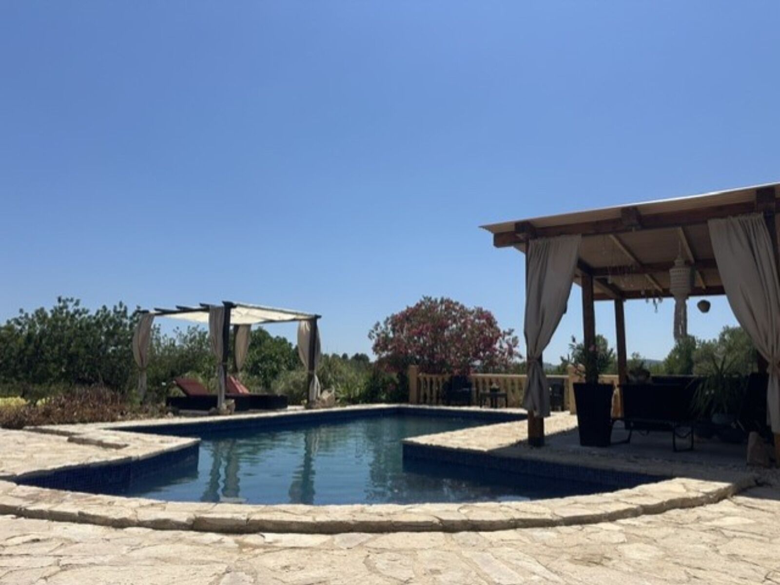 Une piscine bordée de pierres, un espace détente couvert et une structure en forme de pergola.