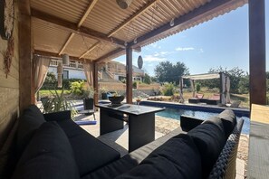A covered outdoor seating area with a pool, wicker furniture, and a view of a building in the background. - Charming Holiday Home near the Sea with Swimming pool (Càlig)