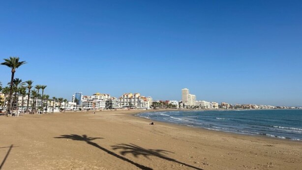 A beach with a clear sky, palm trees, and buildings in the background. - Luxury Holiday Home nearby the Beach with Pool (Càlig)
