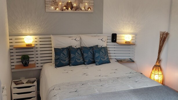 Quarto com cama, mesas de cabeceira, prateleira na parede e luminária pendente.