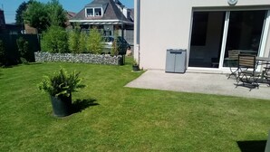 Um quintal bem cuidado com gramado, uma planta em vaso, um muro de pedra e um espaço de pátio com mobiliário para área externa.