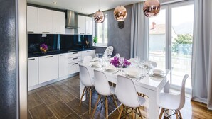 A modern kitchen with white cabinets, a black countertop, and a dining area with white chairs and a table set for four. - Zaton Family Getaway Near Adriatic Sea (Dubrovnik)