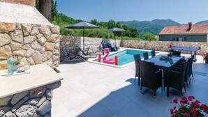 A pool area with lounge chairs, a dining table, and a view of mountains. - Zaton Family Getaway Near Adriatic Sea (Dubrovnik)