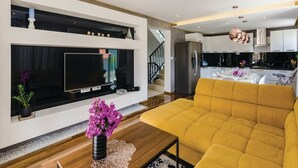 A modern living room with a large flat-screen TV, a yellow sofa, and a dining area with a table set for two. - Zaton Family Getaway Near Adriatic Sea (Dubrovnik)