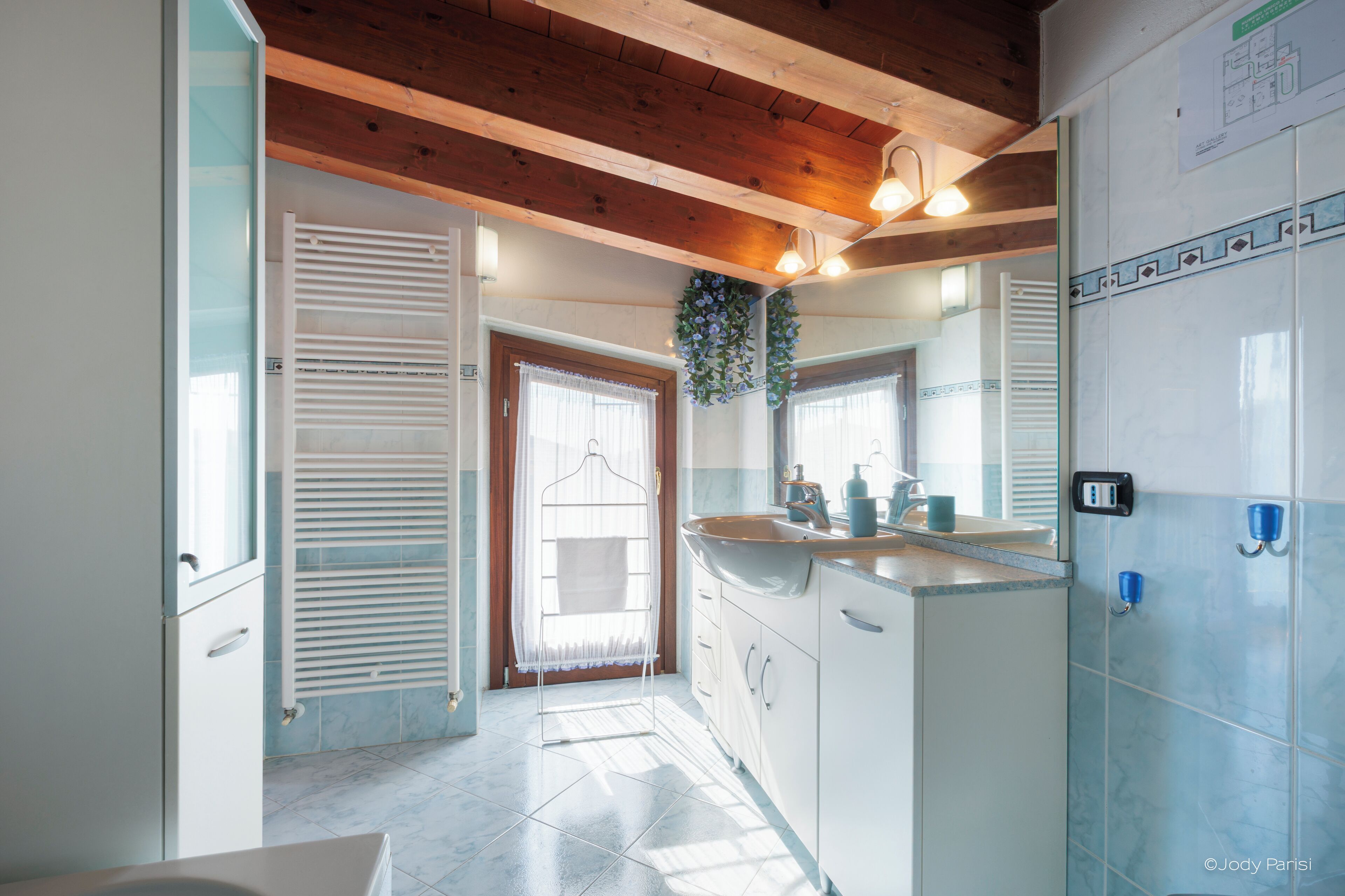 A bathroom with a wooden ceiling, a large mirror, a sink with a soap dispenser, and a towel rack.