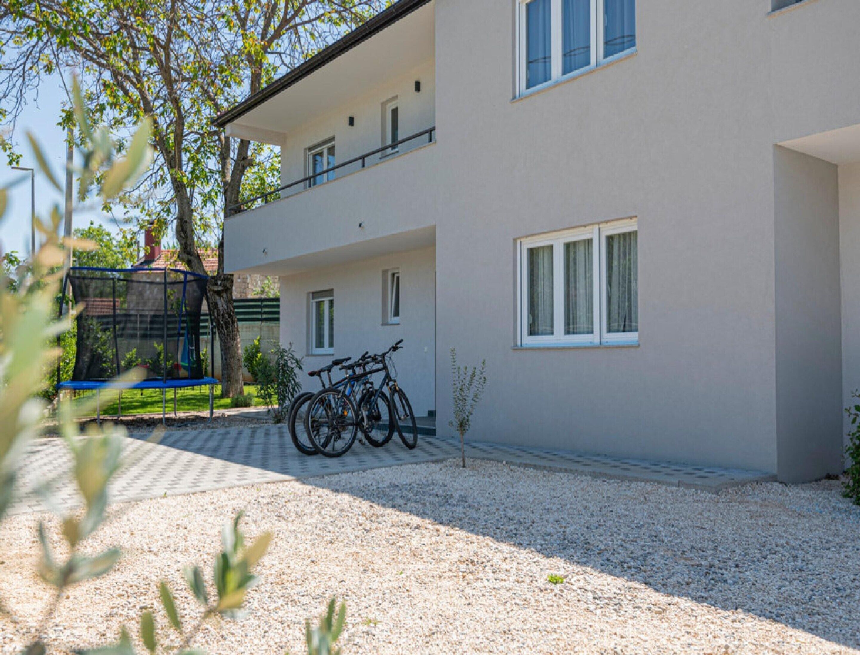 A two-story building with a gravel driveway, a trampoline, and bicycles parked outside.