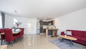 A modern living room with a red sofa, a dining area with red chairs, a kitchen with dark cabinets, and a hallway leading to a door. - Paradise Villa in the Countryside (Imotski)