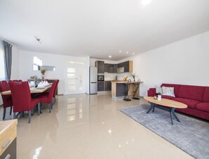 A modern living room with a red sofa, a dining area with red chairs, a kitchen with dark cabinets, and a hallway leading to a door. - Paradise Villa in the Countryside (Imotski)