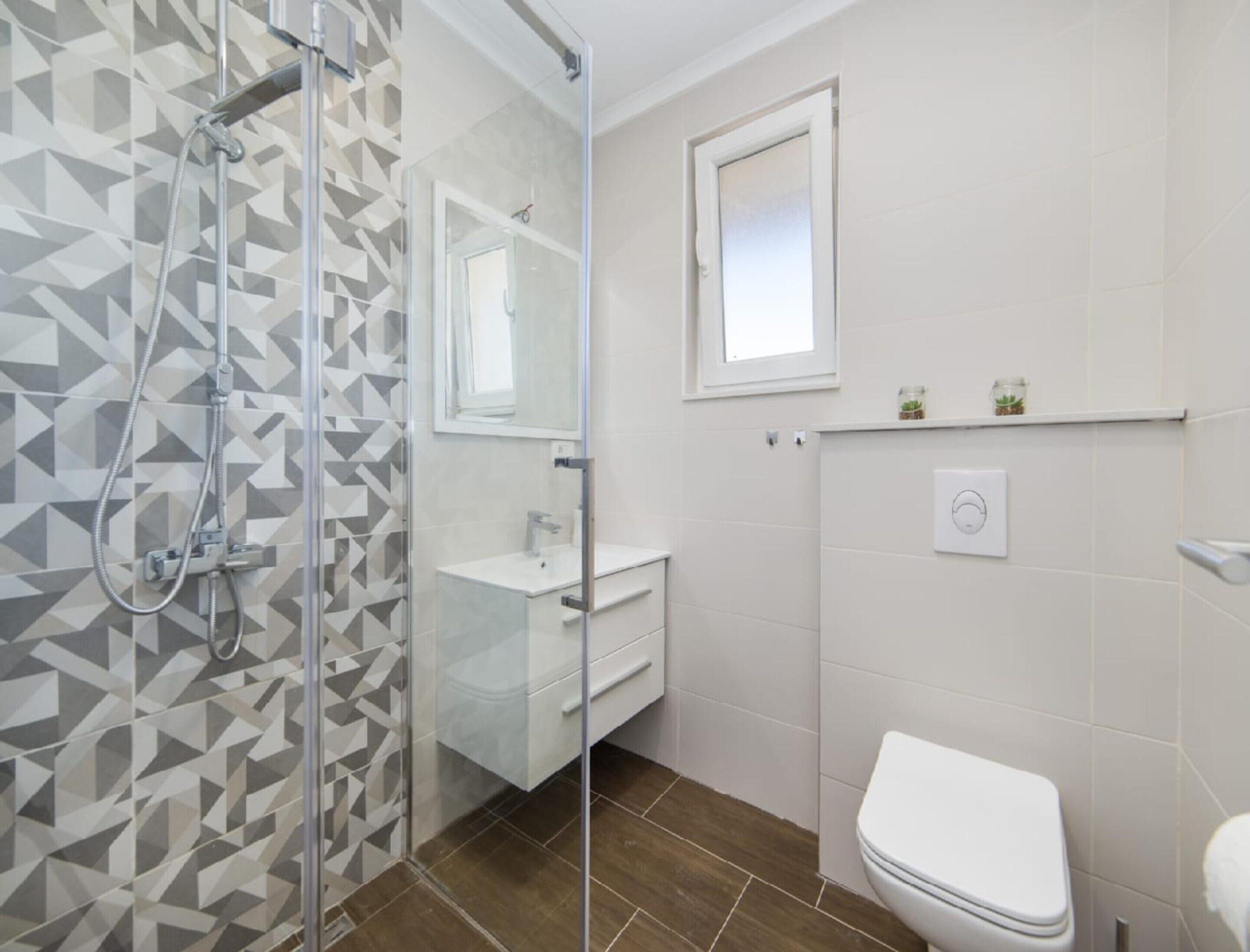 A bathroom with a glass shower enclosure, a white sink, a toilet, and a small window above the sink.