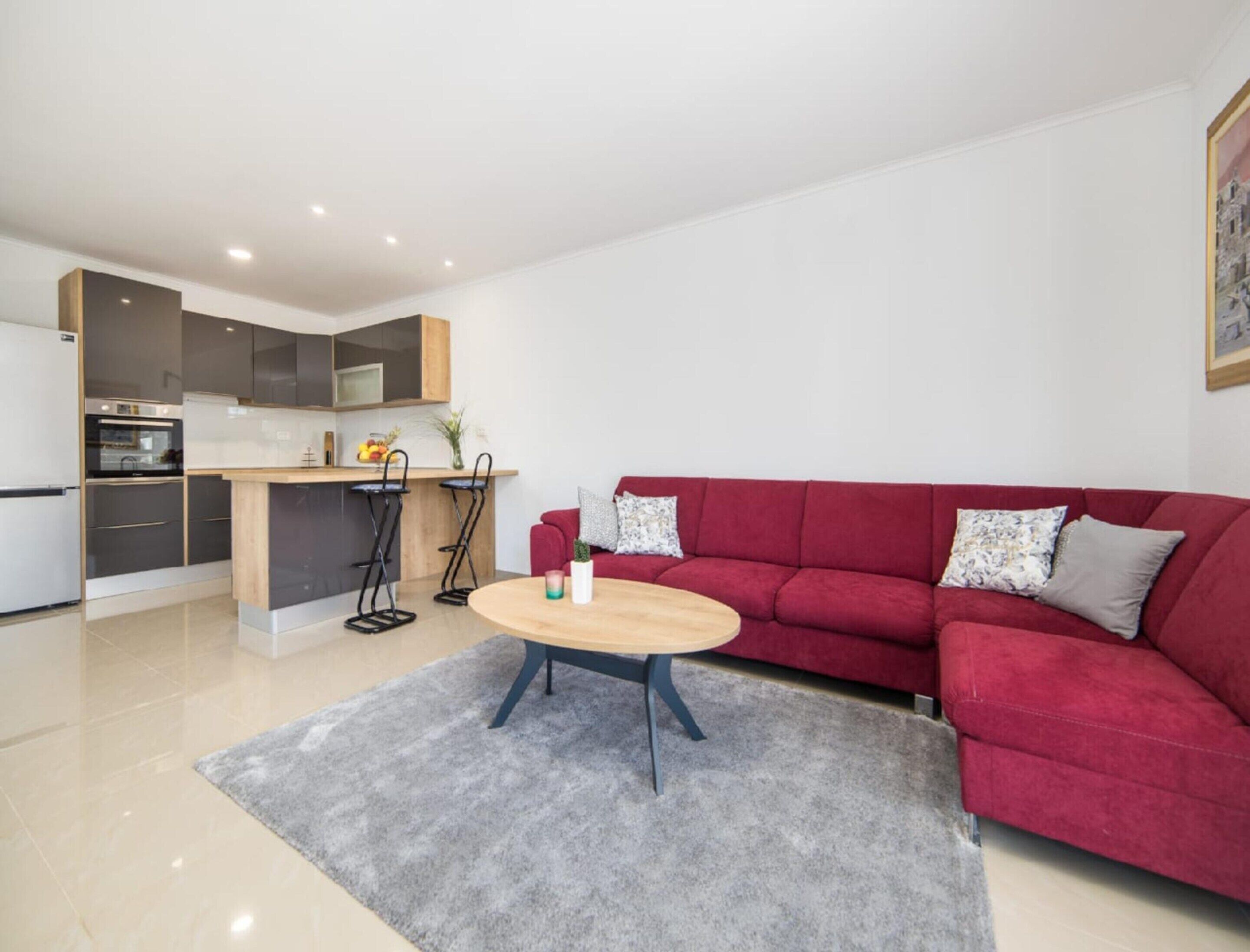 A modern living room with a red sofa, a round coffee table, and a kitchen area with a bar stool.