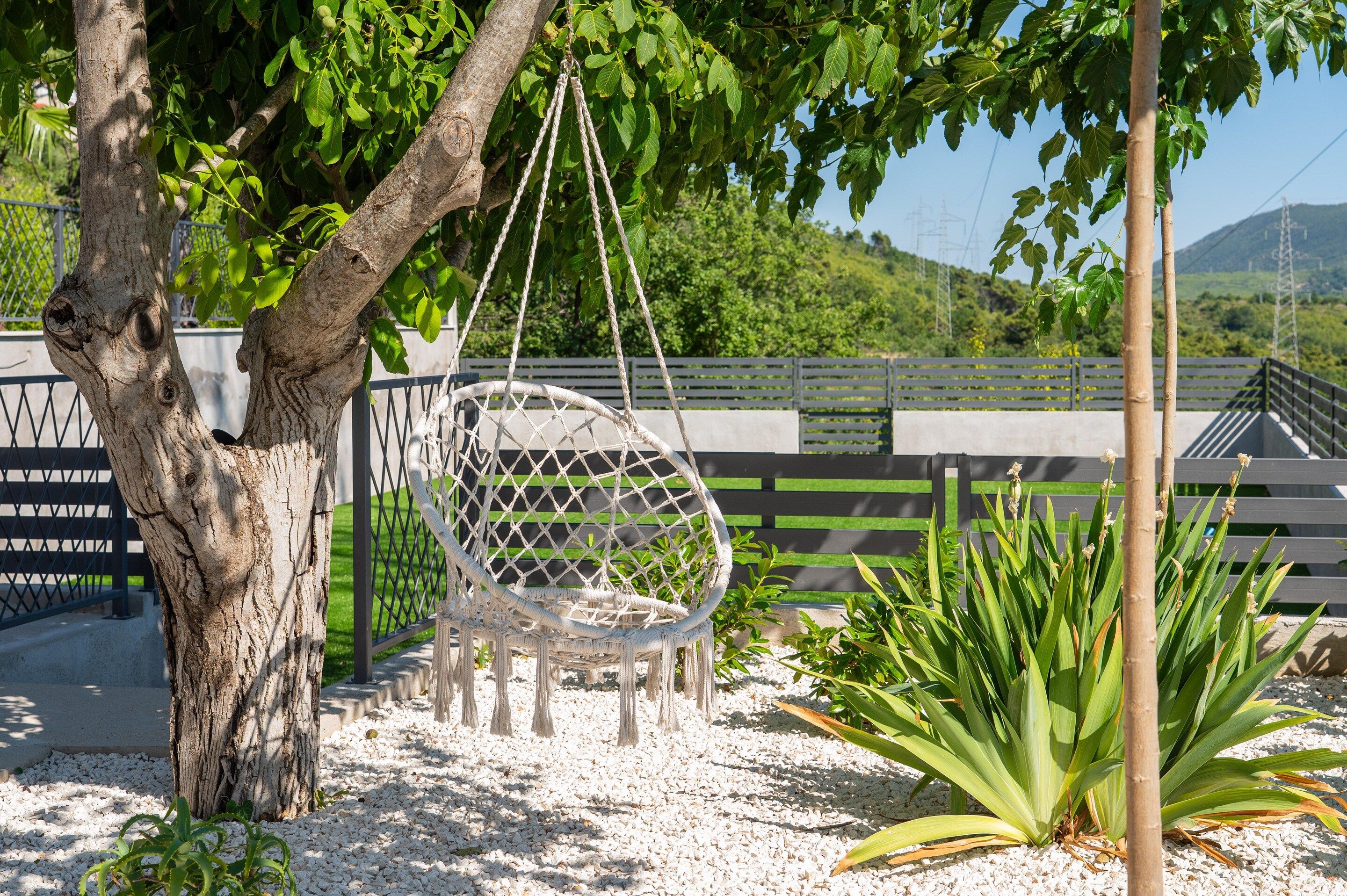 A hammock hanging from a tree, surrounded by greenery and a fence.
