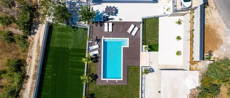 An aerial view of a residential property with a swimming pool, a patio area, and a garage.