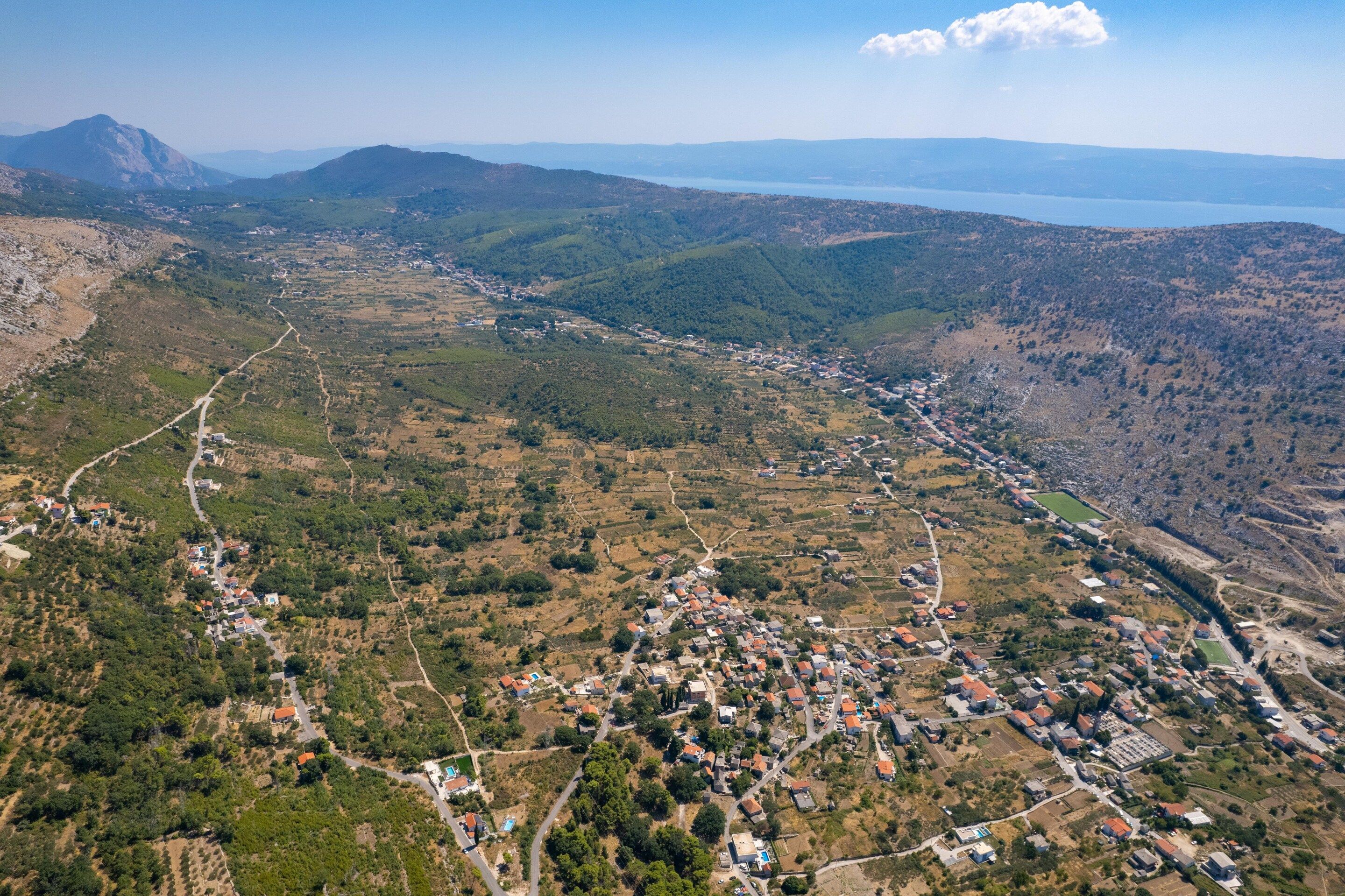 Une vue aérienne d’une ville vallonnée, où se côtoient des zones résidentielles et agricoles, des routes et, au loin, une étendue d’eau.