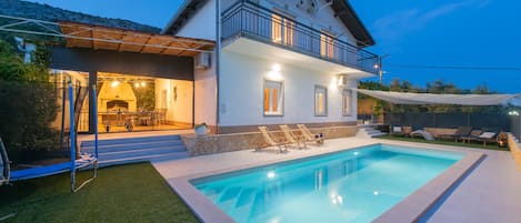 A two-story house with a swimming pool, outdoor seating, and a barbecue area.