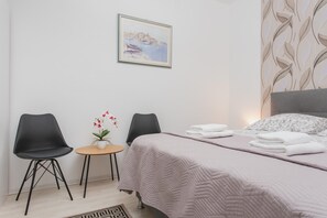 Ein Hotelzimmer mit Bett, zwei Sessel, einem kleinen Tisch mit Topfpflanze und einem Bild an der Wand.