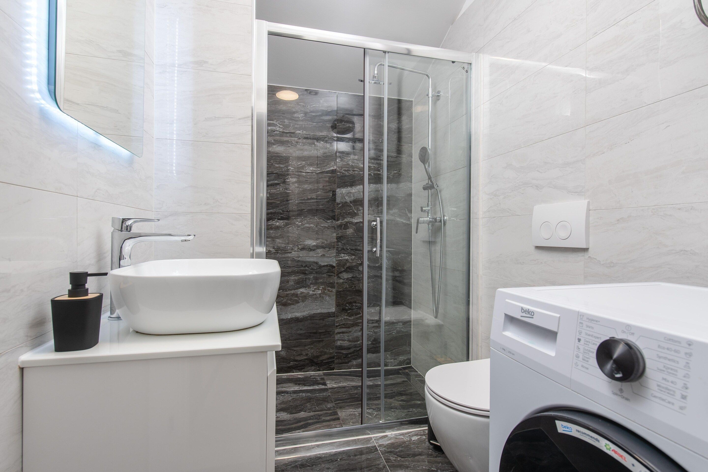 A modern bathroom with a glass-enclosed shower, a white sink, and a toilet.