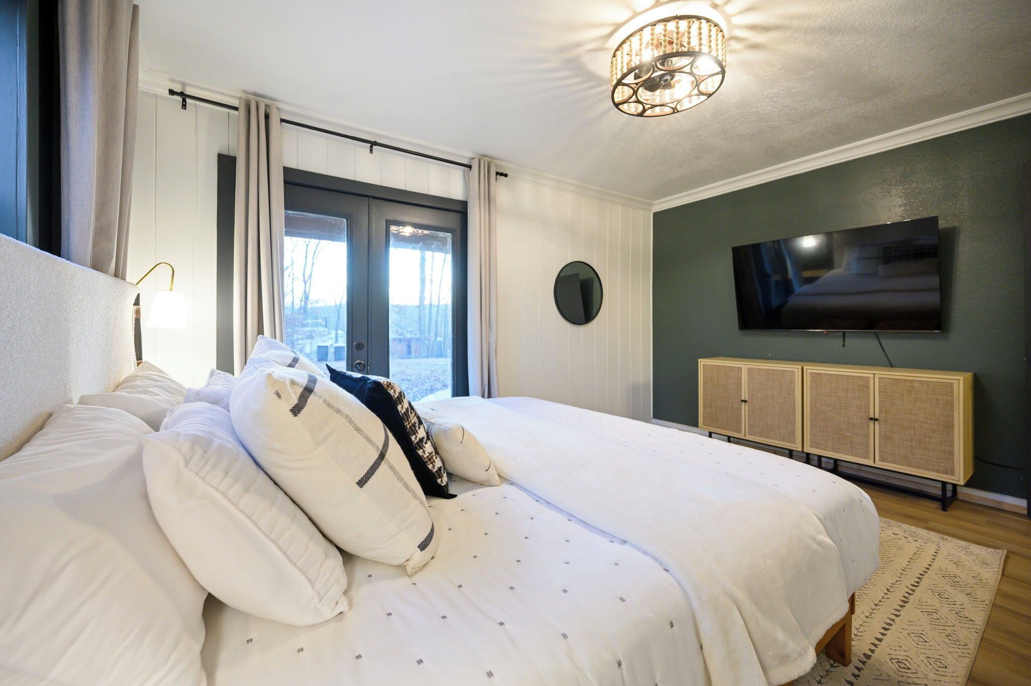 Un dormitorio con una cama grande, un televisor montado en la pared y un ventanal con cortinas.