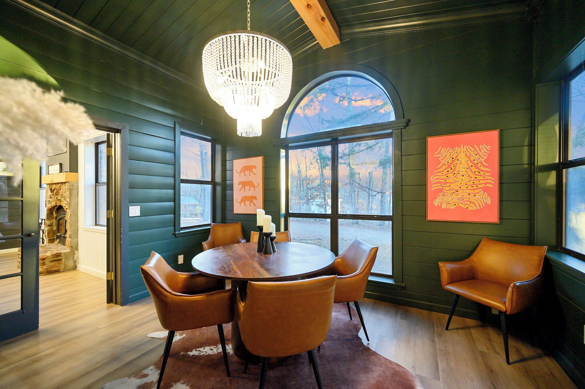 Un comedor con una mesa de madera y sillas de cuero, una araña y obras de arte en las paredes.