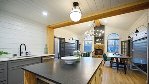 Uma cozinha moderna com ilha central, vigas de madeira e área de jantar com lareira.