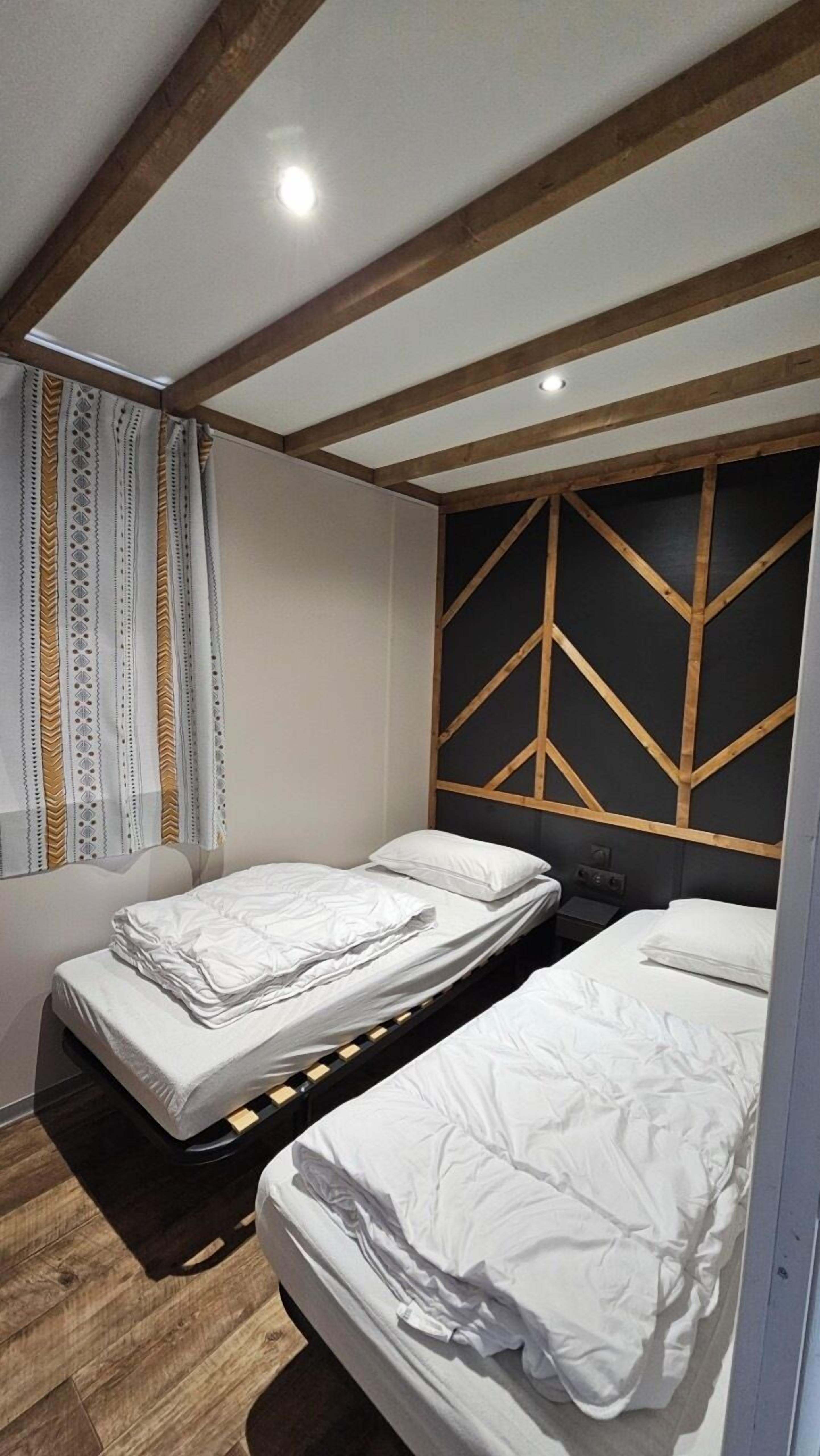 Una habitación con dos camas individuales, vigas de madera en el techo y un panel de pared con diseño geométrico.