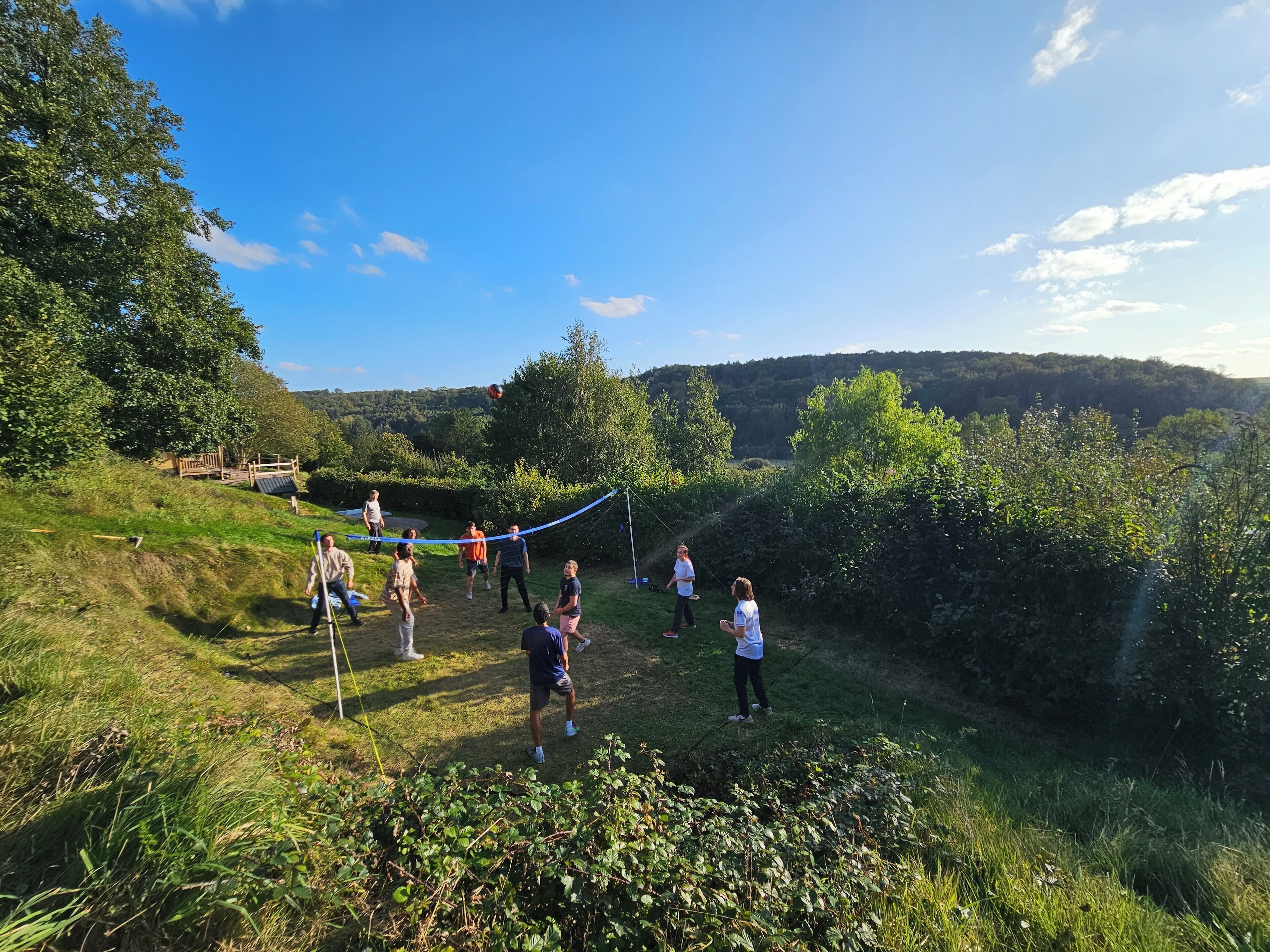 Un groupe de personnes pratiquant un sport sur un terrain herbeux, avec des arbres et des collines en arrière-plan.