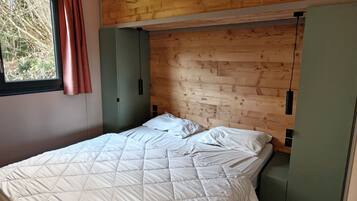 Ein Schlafzimmer mit einem hölzernen Kopfende, einem Bett mit weißer, gesteppter Bettdecke, einem Fenster mit Vorhang und einem grünen Kleiderschrank.
