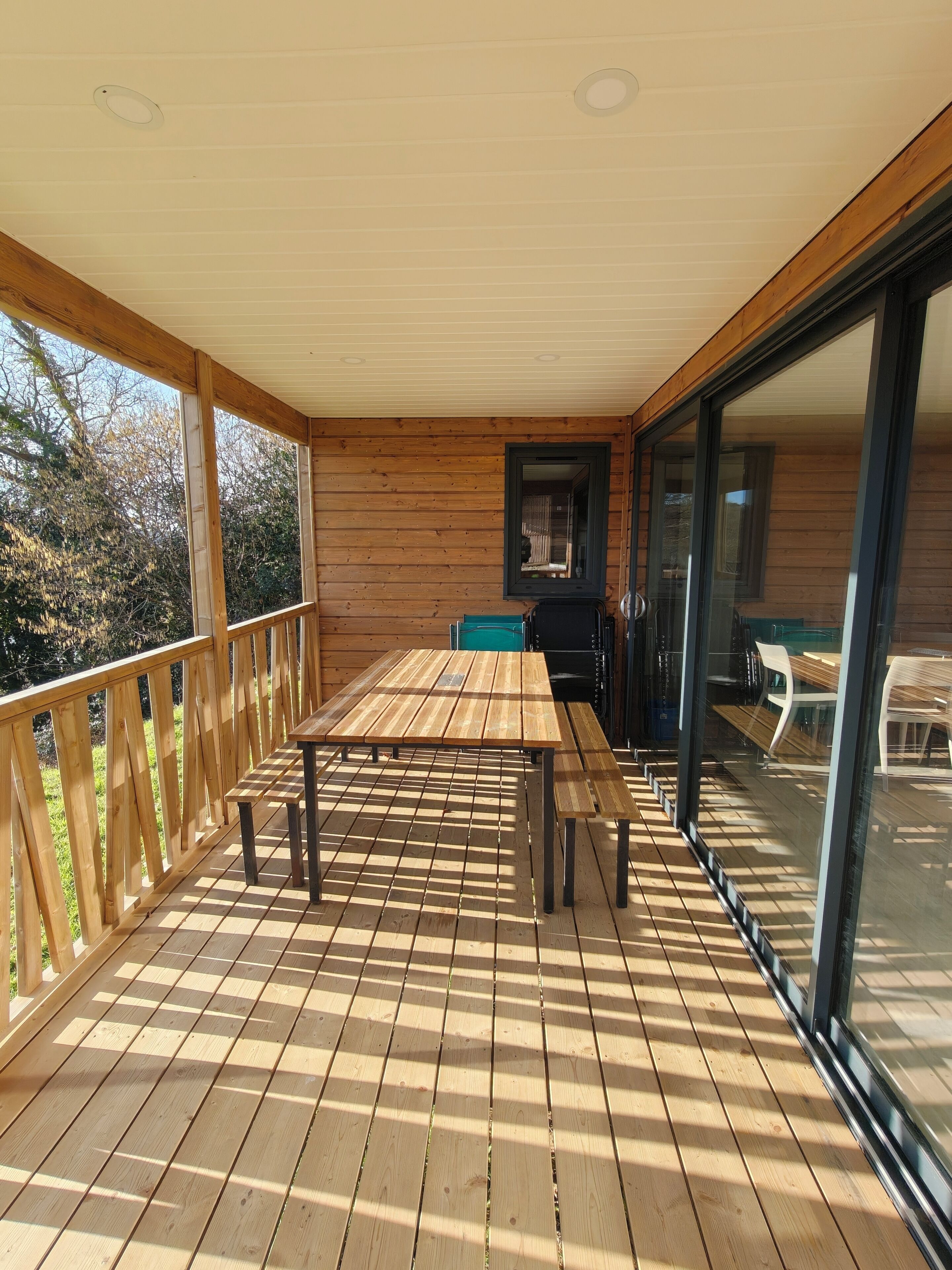 A wooden deck with a table and chairs, a sliding glass door, and a view of the outdoors.