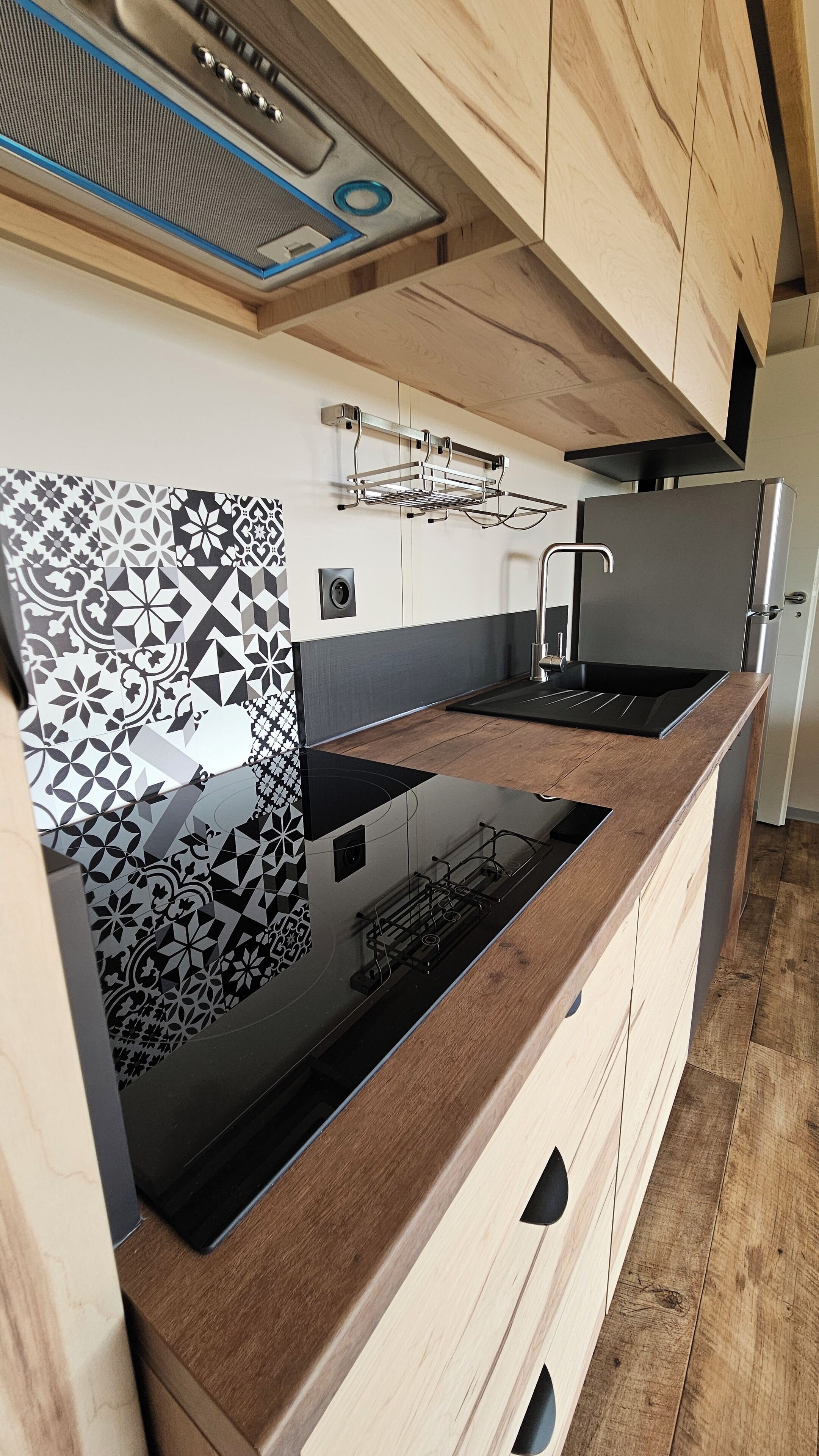 A modern kitchen with a black countertop, wooden cabinets, and a patterned backsplash.