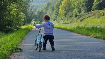 Un bambino che va in bicicletta su una strada asfaltata, circondato da una vegetazione rigogliosa e colline.