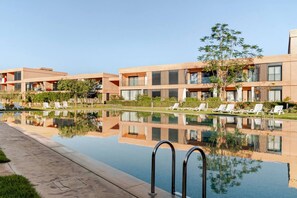 Um hotel moderno com piscina, espreguiçadeiras e um reflexo nítido na água.