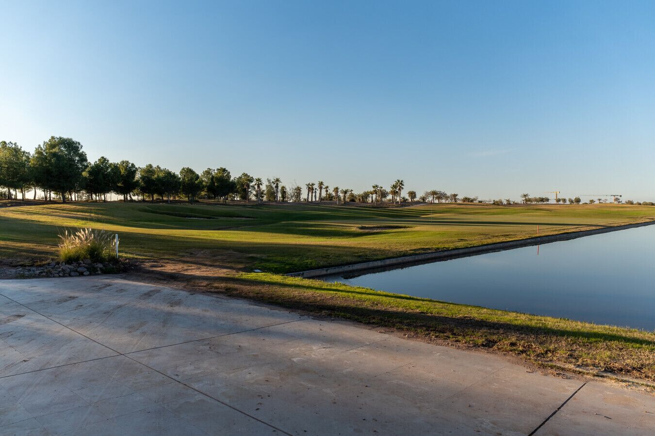A golf course with a water feature, trees, and a clear sky.