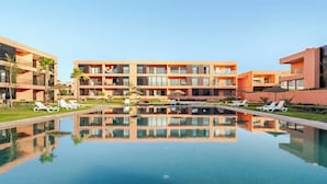 Ein modernes Hotel mit einem zentralen Pool, mehreren Balkonen und Liegestühlen.