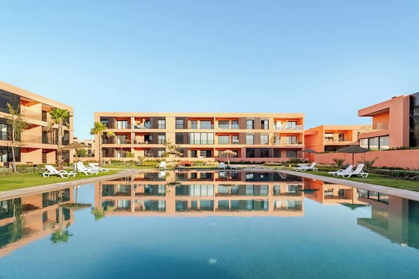 Um hotel moderno com piscina central, várias varandas e espreguiçadeiras.