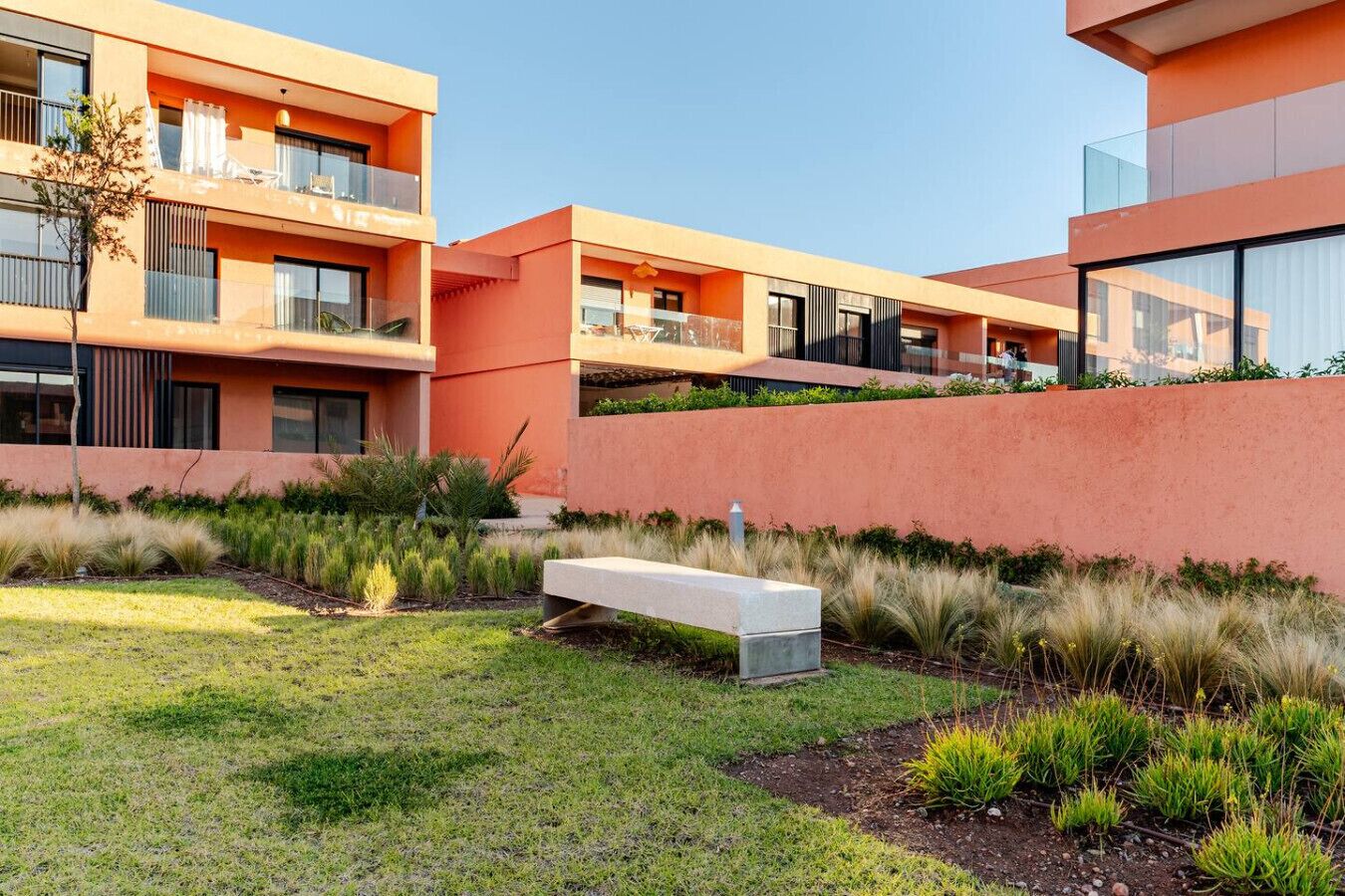 A modern building with balconies, a grassy area, and a bench.