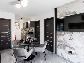 A modern kitchen with a marble backsplash, a dining area with grey upholstered chairs, and a flat-screen TV mounted on the wall. - Serene Family Villa by the Rogoznica Coast (Rogoznica)