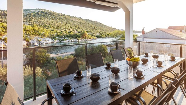 A dining table set with cups, bowls, and glasses, overlooking a river and hills. - Serene Family Villa by the Rogoznica Coast (Rogoznica)