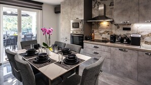 A modern kitchen with a dining area, featuring a large island, built-in appliances, and a view through the glass doors. - Serene Family Villa by the Rogoznica Coast (Rogoznica)