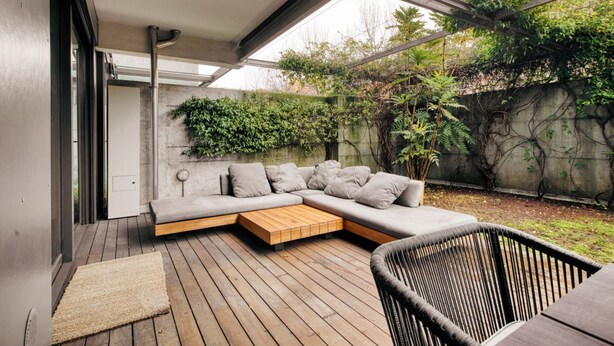 A modern outdoor living space with a sectional sofa, a wooden coffee table, and a wicker chair. - Hostmate - Milano - Ulpio Traiano (Milano)