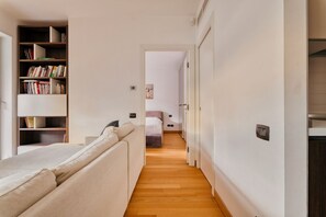 Ein schmaler Flur mit einem Bett, einem Bücherregal und einer Tür zu einem anderen Raum.
