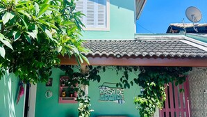 A two-story building with a green facade and a tiled roof. There is a bench under a covered area with a sign that reads "CASADE DE BRAIA". - Cozy and charming house 300 meters from Indaiá Beach, in Bertioga. (Bertioga)