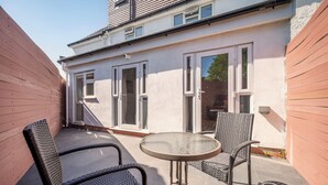 A patio with two chairs and a table, a white building with large windows, and a wooden fence. - Modern Luxury 4Bdrm 15 min to LDN centre | Business/Vacay | Parking onsite (London)