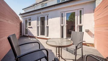 Une terrasse avec deux chaises et une table, un bâtiment blanc doté de grandes fenêtres et une clôture en bois.