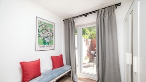 A room with a bench, red pillows, a framed artwork, grey curtains, and a view through a glass door. - Modern Luxury 4Bdrm 15 min to LDN centre | Business/Vacay | Parking onsite (London)